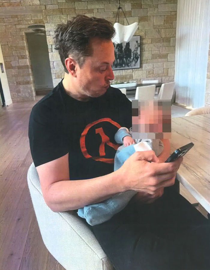 Man holding a baby while looking at his phone, seated in a modern living room setting. Man holding a baby while looking at his phone, seated in a modern living room setting.