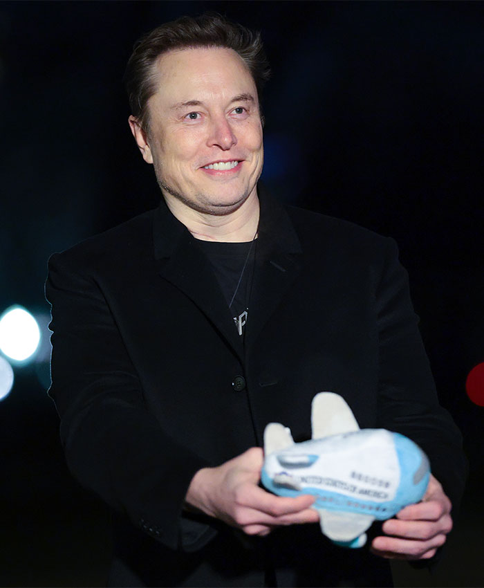 Elon Musk smiling while holding a toy rocket, wearing a black jacket at a public event. Elon Musk smiling while holding a toy rocket, wearing a black jacket at a public event.