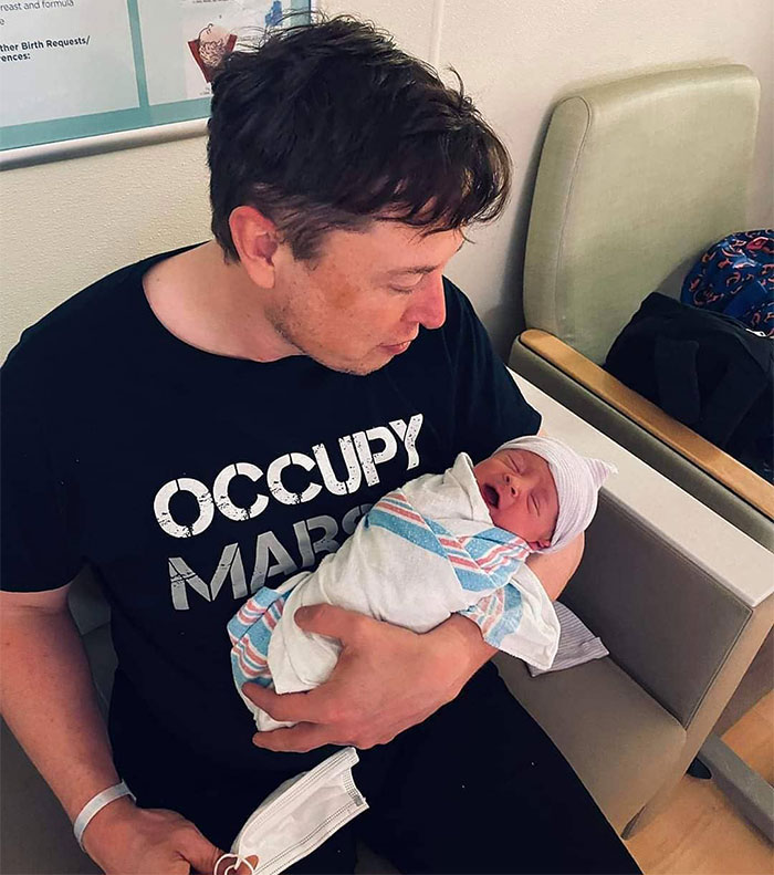 A person in a black shirt holds a newborn in a hospital setting, highlighting a family moment. A person in a black shirt holds a newborn in a hospital setting, highlighting a family moment.