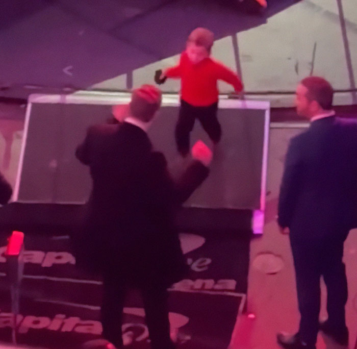 Elon Musk in a suit on stage with a child in a red shirt, related to discussions of leaving behind son X. Elon Musk in a suit on stage with a child in a red shirt, related to discussions of leaving behind son X.