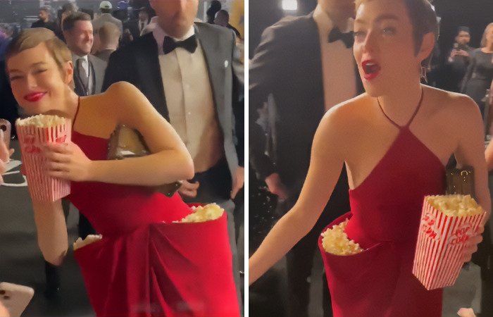 Emma Stone in a red dress with popcorn pockets at an event, surrounded by people in formal attire. Emma Stone in a red dress with popcorn pockets at an event, surrounded by people in formal attire.
