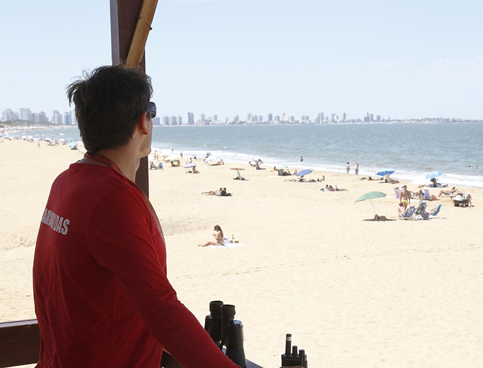 Lifeguard in red shirt overlooking a sunny beach with city skyline in the distance on a clear day. Lifeguard in red shirt overlooking a sunny beach with city skyline in the distance on a clear day.