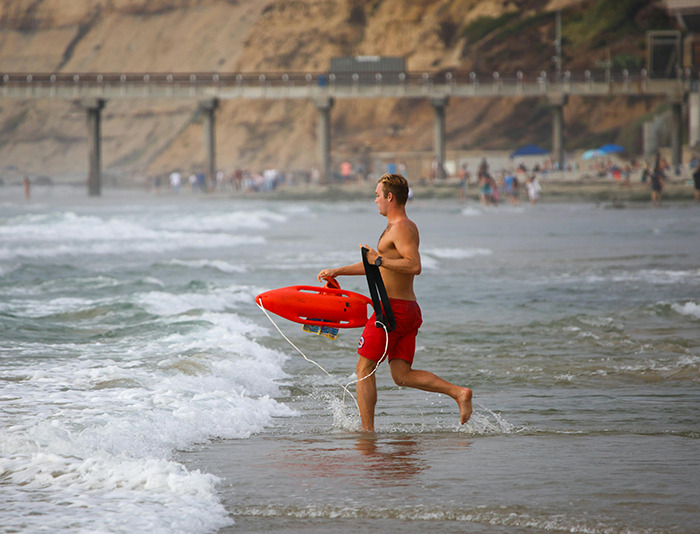 A lifeguard in red shorts holding a lifesaver, running into the ocean. A lifeguard in red shorts holding a lifesaver, running into the ocean.