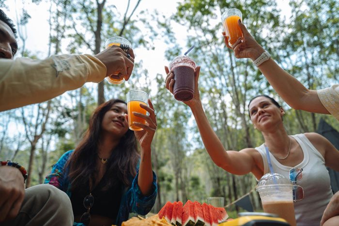 Friends raising glasses in a forest picnic setting with food, highlighting a social gathering with a serial moocher theme. Friends raising glasses in a forest picnic setting with food, highlighting a social gathering with a serial moocher theme.