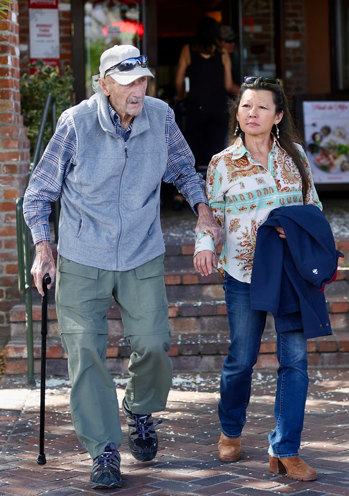 An elderly man and a woman walking together outdoors, with the man using a cane for support. An elderly man and a woman walking together outdoors, with the man using a cane for support.