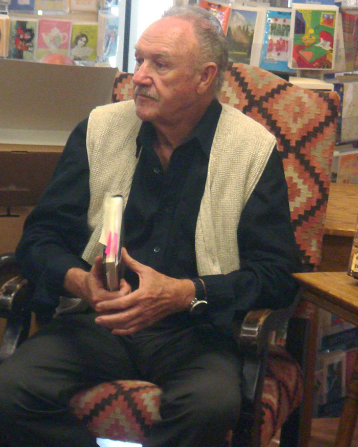 Man in a patterned chair holding a book, seated in a bookstore setting. Man in a patterned chair holding a book, seated in a bookstore setting.