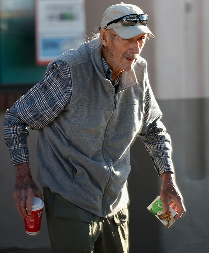 Elderly man in casual attire holding a coffee cup and snack, walking outside on a sunny day. Elderly man in casual attire holding a coffee cup and snack, walking outside on a sunny day.