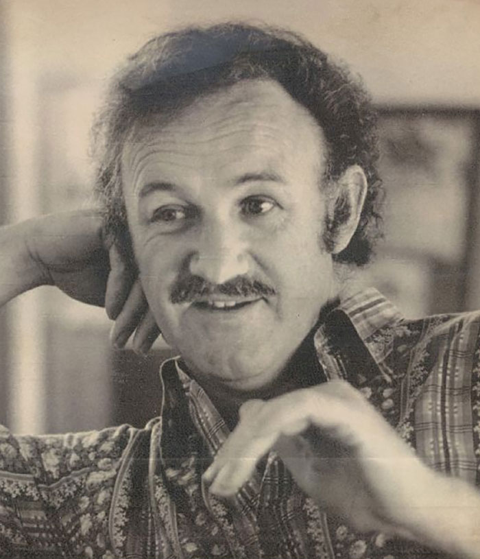 An older image of Gene Hackman smiling in a casual shirt, gesturing with a relaxed demeanor. An older image of Gene Hackman smiling in a casual shirt, gesturing with a relaxed demeanor.