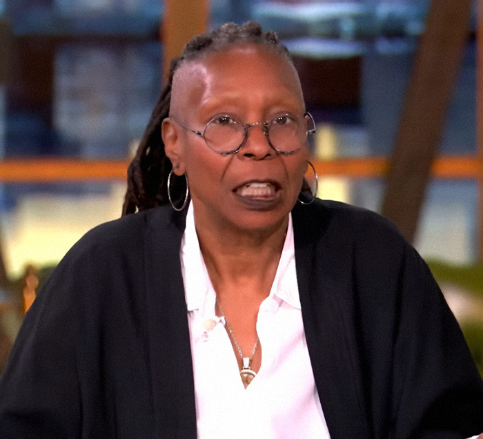 Whoopi Goldberg wearing glasses and earrings speaking on a TV set. Whoopi Goldberg wearing glasses and earrings speaking on a TV set.