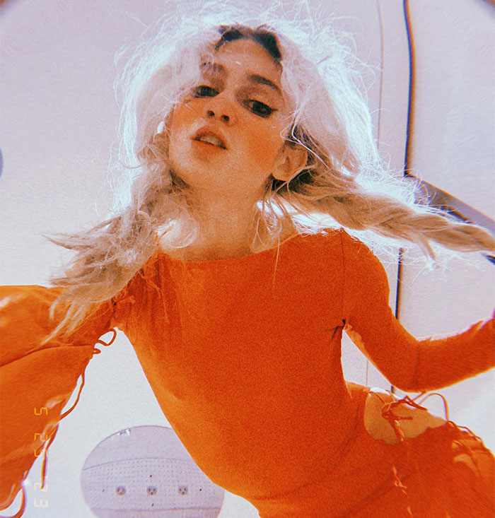 Young woman with long hair in a bright orange outfit, looking upwards toward the camera. Young woman with long hair in a bright orange outfit, looking upwards toward the camera.