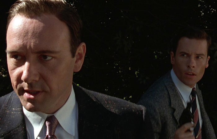 Kevin Spacey and Guy Pearce as characters in suits, one in focus, appearing in a tense outdoor scene. Kevin Spacey and Guy Pearce as characters in suits, one in focus, appearing in a tense outdoor scene.