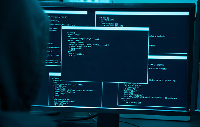 Stock photo of hacker in front of computer screen showing code. Stock photo of hacker in front of computer screen showing code.