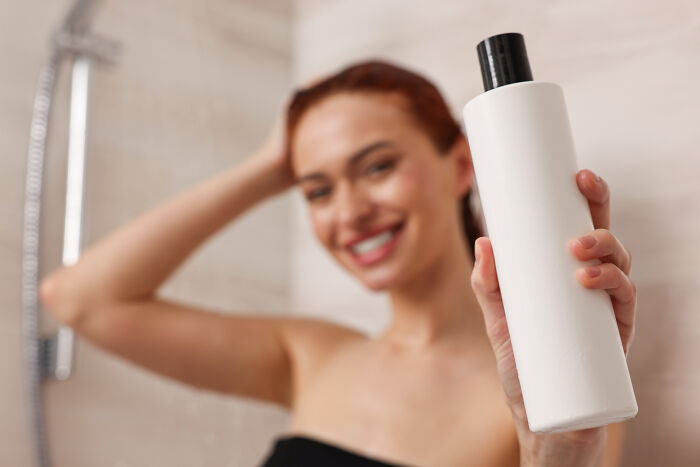 Person holding a multi-functional bottle, smiling in a bathroom setting.