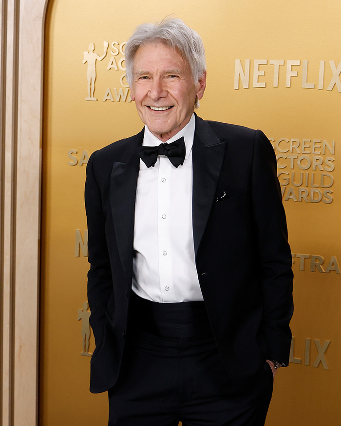 Harrison Ford in a suit smiling at a red carpet. Harrison Ford in a suit smiling at a red carpet.
