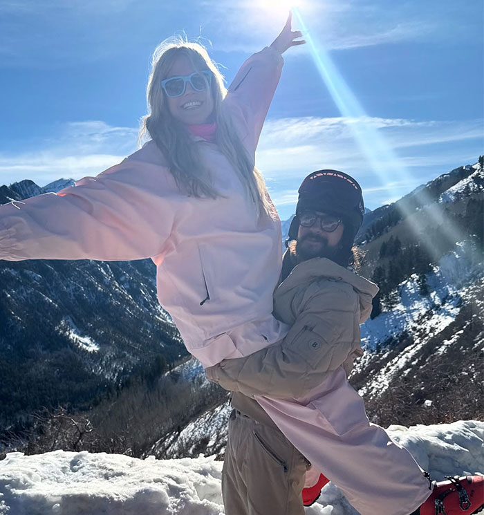 Heidi Klum in a snowy landscape, wearing a pink outfit, smiling, lifted by a man in a beige outfit. Heidi Klum in a snowy landscape, wearing a pink outfit, smiling, lifted by a man in a beige outfit.
