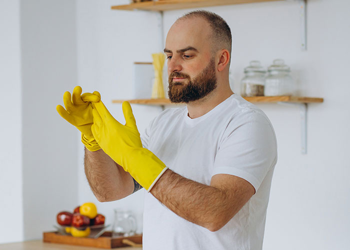 Man in a white shirt putting on yellow cleaning gloves, illustrating a response to being called unhelpful in household chores. Man in a white shirt putting on yellow cleaning gloves, illustrating a response to being called unhelpful in household chores.