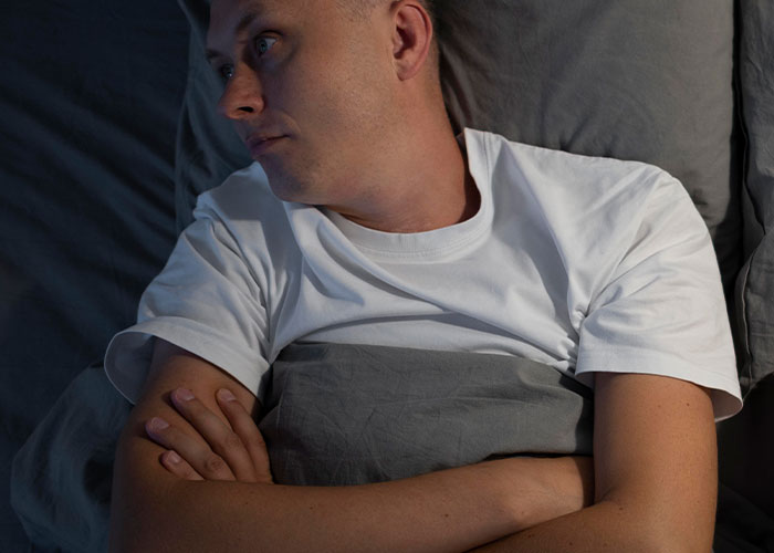 Man in bed with folded arms, looking thoughtful, highlighting the theme of being unhelpful in relationships. Man in bed with folded arms, looking thoughtful, highlighting the theme of being unhelpful in relationships.