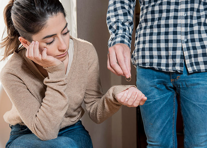 Woman looking pensive while a man holding a ring stands next to her, highlighting an unhelpful relationship dynamic. Woman looking pensive while a man holding a ring stands next to her, highlighting an unhelpful relationship dynamic.