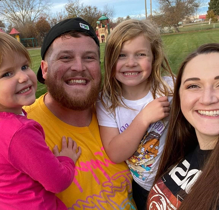 Happy family in a park setting, featuring a husband, wife, and their two daughters smiling at the camera. Happy family in a park setting, featuring a husband, wife, and their two daughters smiling at the camera.