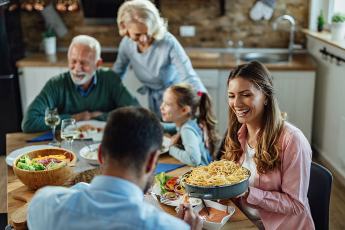 Happy family dinner, woman serving pasta, reflecting dynamic of mother-in-law being asked to leave for bringing uninvited guest. Happy family dinner, woman serving pasta, reflecting dynamic of mother-in-law being asked to leave for bringing uninvited guest.
