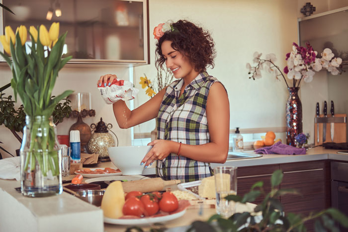 Woman cooking in a stylish kitchen with flowers, engaging in meal preparation, related to MIL and DIL dinner story. Woman cooking in a stylish kitchen with flowers, engaging in meal preparation, related to MIL and DIL dinner story.