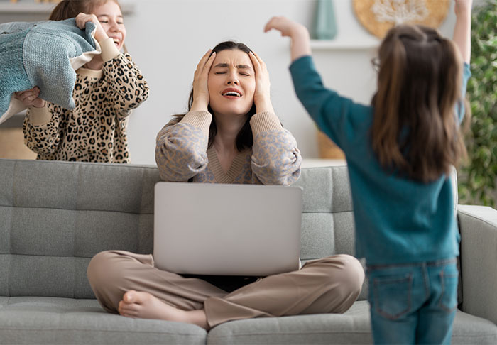 A stressed woman with a laptop on a couch as children play loudly around her, highlighting time management challenges at home. A stressed woman with a laptop on a couch as children play loudly around her, highlighting time management challenges at home.