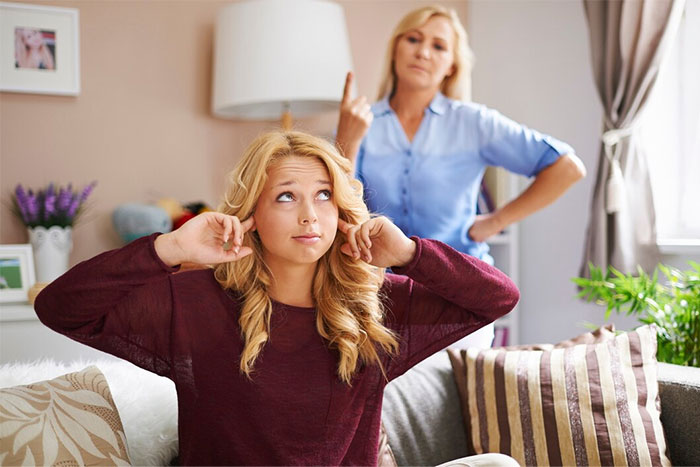 Mother scolding daughter covering ears in living room, expressing dislike for her name selected from Bible. Mother scolding daughter covering ears in living room, expressing dislike for her name selected from Bible.