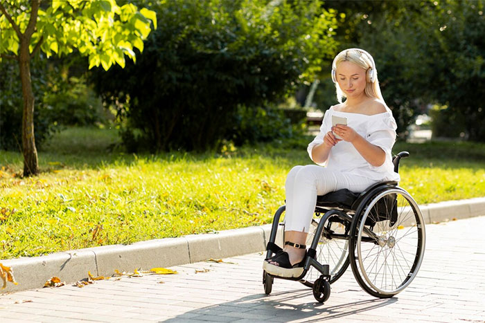 Woman in wheelchair outside, wearing headphones, reading a book, enjoying a sunny day with trees and grass around. Woman in wheelchair outside, wearing headphones, reading a book, enjoying a sunny day with trees and grass around.