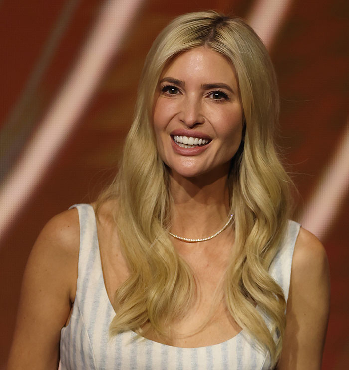 Blonde woman smiling with long hair extensions, wearing a striped dress and a necklace, in front of a warm background. Blonde woman smiling with long hair extensions, wearing a striped dress and a necklace, in front of a warm background.