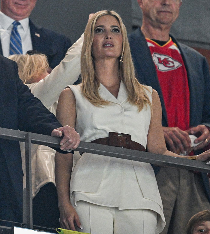 Ivanka Trump with long hair extensions at an event, wearing a white outfit, surrounded by people in a sports setting. Ivanka Trump with long hair extensions at an event, wearing a white outfit, surrounded by people in a sports setting.