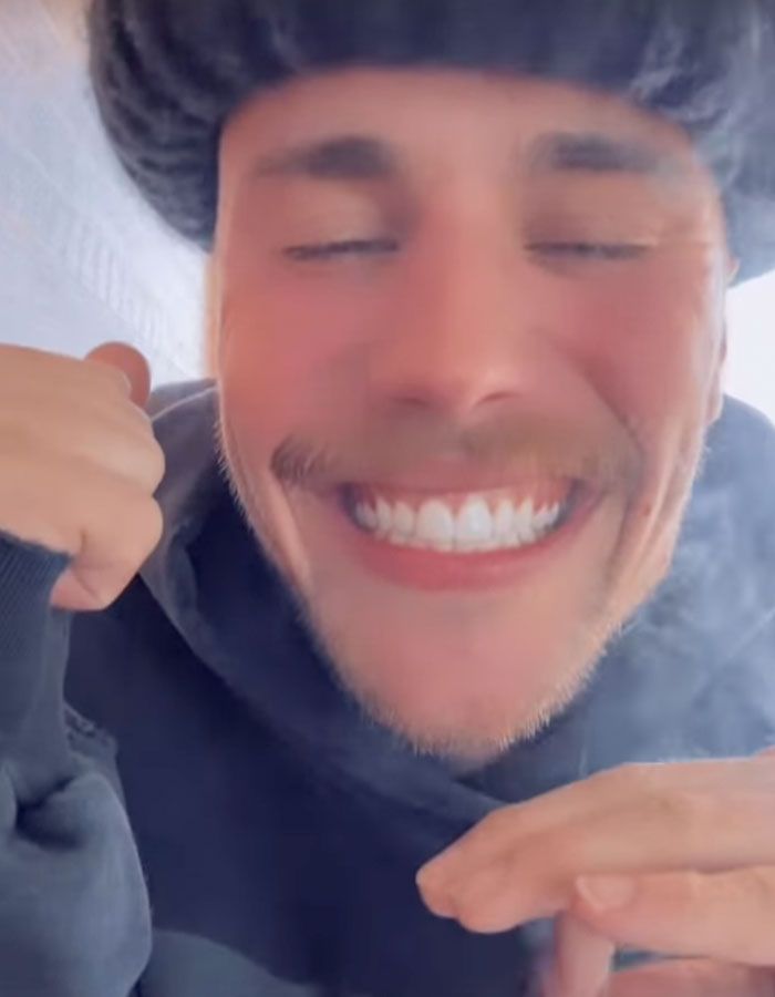 Young man smiling with eyes closed, wearing a dark hoodie indoors, smoke visible around him. Young man smiling with eyes closed, wearing a dark hoodie indoors, smoke visible around him.