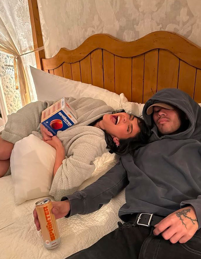 Two people relaxing on a bed, one holding a canned drink, smiling and enjoying a casual moment. Two people relaxing on a bed, one holding a canned drink, smiling and enjoying a casual moment.