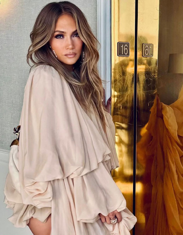 Elegant woman in a beige dress posing near a reflective golden surface, styled by celebrity hairstylist Jesus Guerrero. Elegant woman in a beige dress posing near a reflective golden surface, styled by celebrity hairstylist Jesus Guerrero.