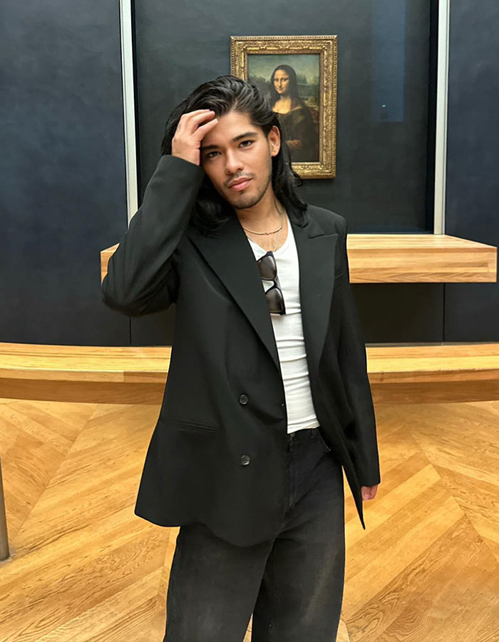 Celebrity hairstylist in a black suit poses in a gallery setting with a famous painting in the background. Celebrity hairstylist in a black suit poses in a gallery setting with a famous painting in the background.