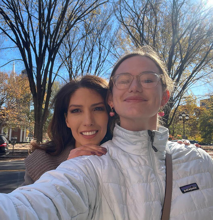 Two women smiling outdoors, one wearing glasses and a white jacket. Two women smiling outdoors, one wearing glasses and a white jacket.