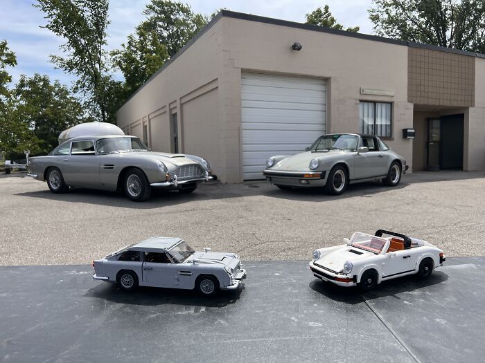Vintage cars parked outside a garage with two toy replicas in the foreground.