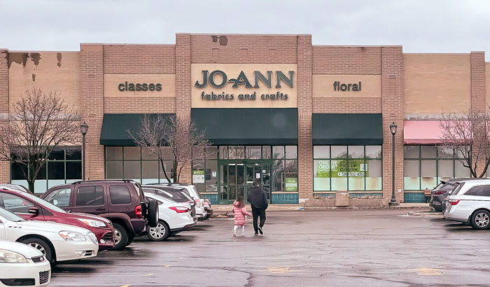 Joann Fabric and Craft store exterior, with people walking, showing brick facade and parking area. Joann Fabric and Craft store exterior, with people walking, showing brick facade and parking area.