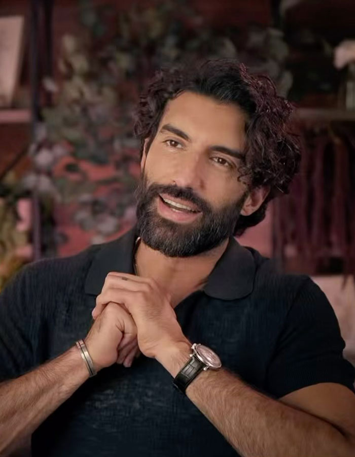 Young man with a beard, wearing a dark shirt and watch, smiling warmly in a cozy setting. Young man with a beard, wearing a dark shirt and watch, smiling warmly in a cozy setting.