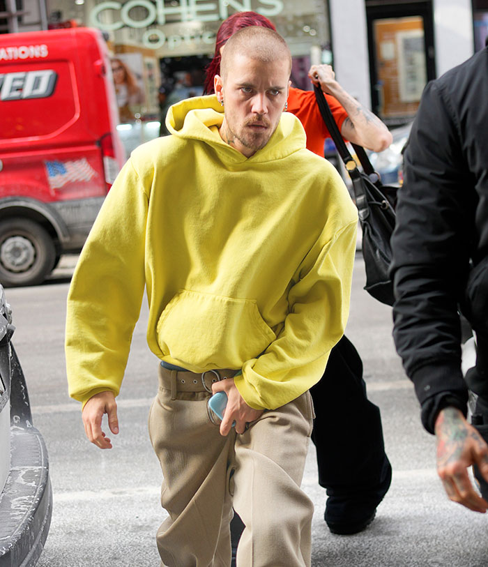 A person in a yellow hoodie and beige pants walks on a city street, holding a phone. A person in a yellow hoodie and beige pants walks on a city street, holding a phone.