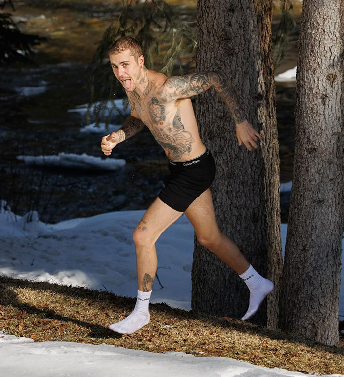 Man running in snow, shirtless and in black shorts, with tattoos visible, near a tree. Man running in snow, shirtless and in black shorts, with tattoos visible, near a tree.
