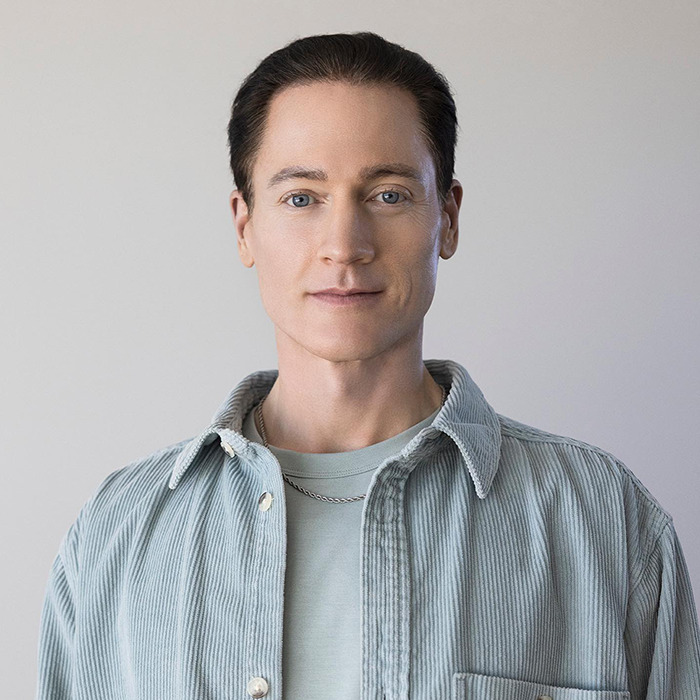 Bryan Johnson in a light blue shirt standing against a plain wall. Bryan Johnson in a light blue shirt standing against a plain wall.