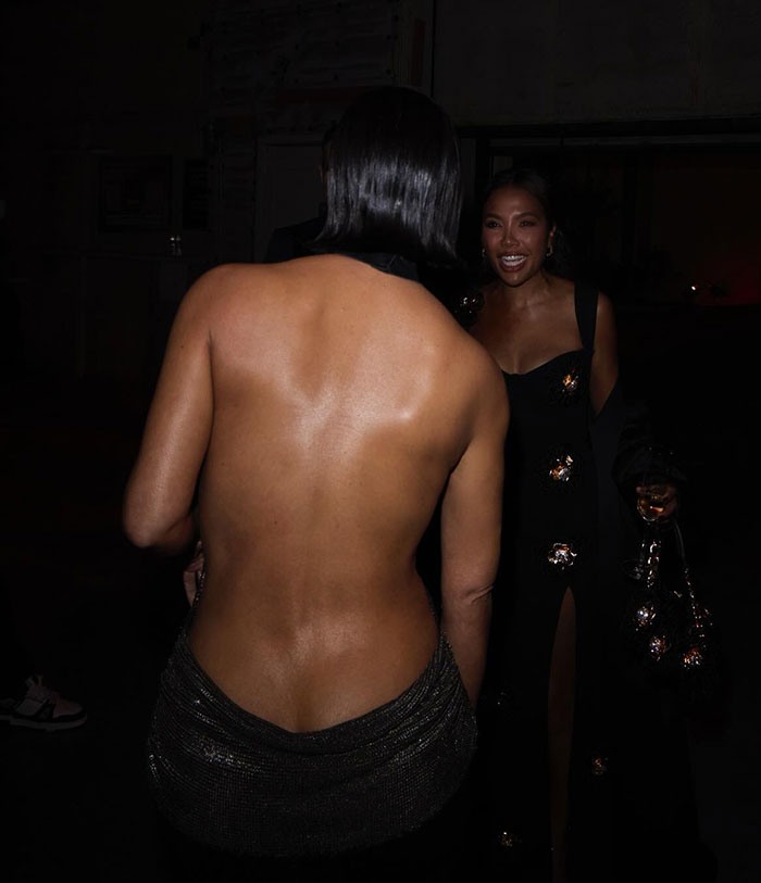 Two women in elegant evening attire at a social event, one in a backless dress, smiling. Two women in elegant evening attire at a social event, one in a backless dress, smiling.