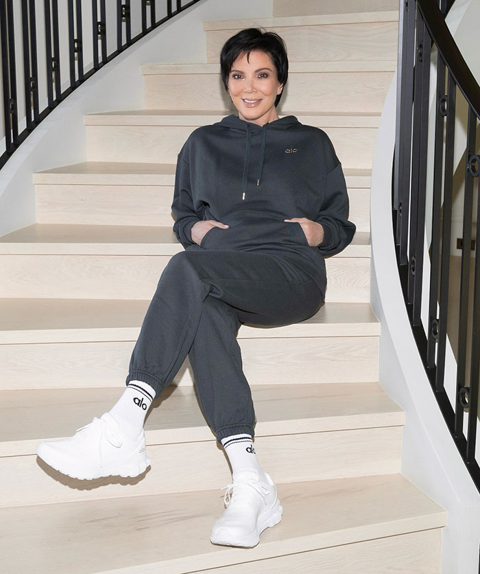 Momager seated on staircase in a dark tracksuit and white sneakers. Momager seated on staircase in a dark tracksuit and white sneakers.