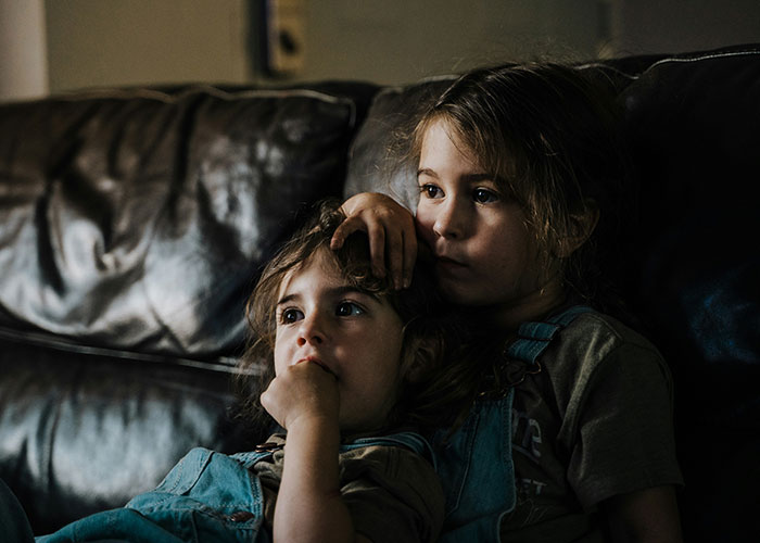 Children sitting on a couch in a dimly lit room, looking thoughtful. Children sitting on a couch in a dimly lit room, looking thoughtful.