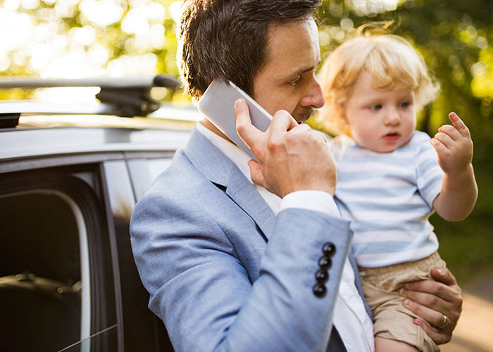 Man in blue suit holding a child, talking on phone outdoors, illustrating family dynamics. Man in blue suit holding a child, talking on phone outdoors, illustrating family dynamics.