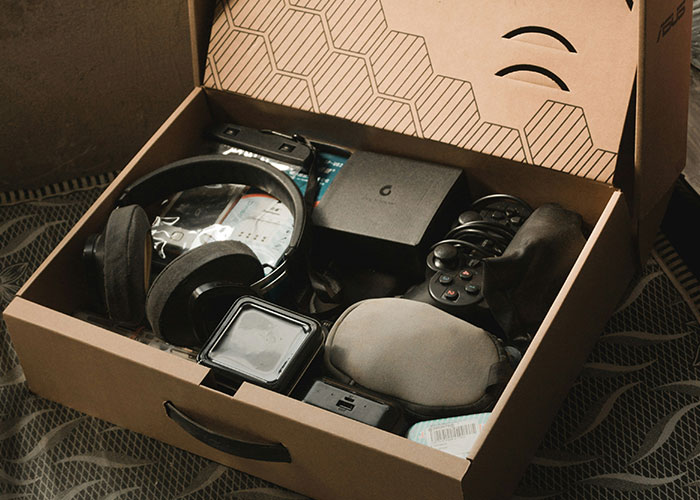 Open box with electronics and gaming items, including a headset and controllers, on a textured surface. Open box with electronics and gaming items, including a headset and controllers, on a textured surface.