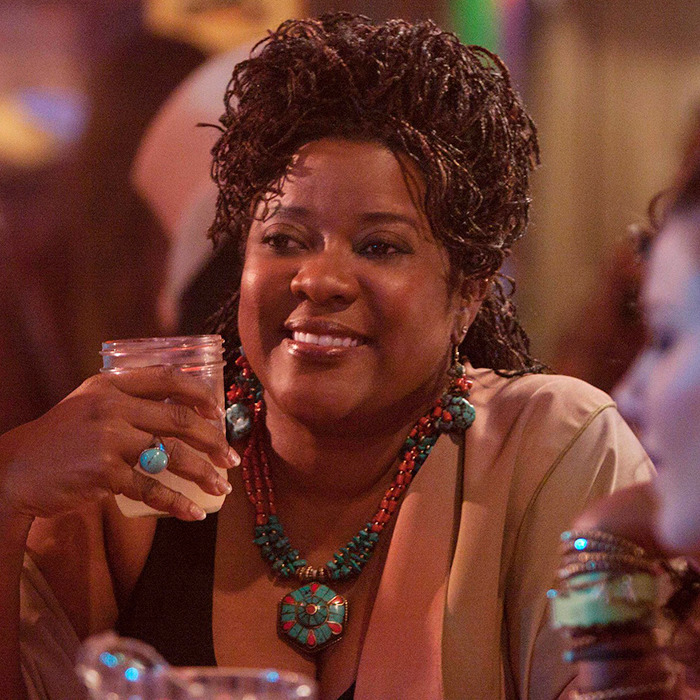 Loretta Devine smiling, holding a drink, adorned with turquoise jewelry, in a dimly lit setting in a scene from "The Client List. Loretta Devine smiling, holding a drink, adorned with turquoise jewelry, in a dimly lit setting in a scene from "The Client List.