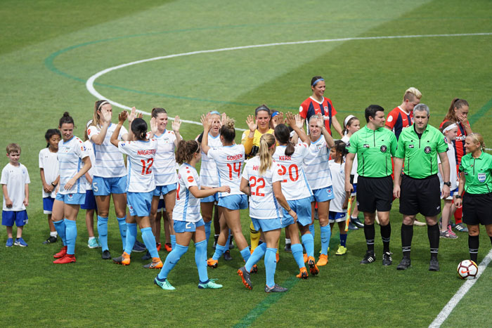 Women’s football team on the field celebrating before a match, with referees standing nearby. Women’s football team on the field celebrating before a match, with referees standing nearby.