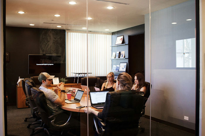 People in a modern office meeting room, discussing around a table with laptops. People in a modern office meeting room, discussing around a table with laptops.