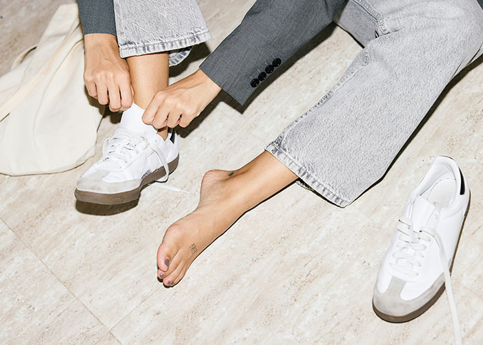 Woman sitting on floor, wearing gray pants, as she removes white sneakers highlighting house rule context. Woman sitting on floor, wearing gray pants, as she removes white sneakers highlighting house rule context.
